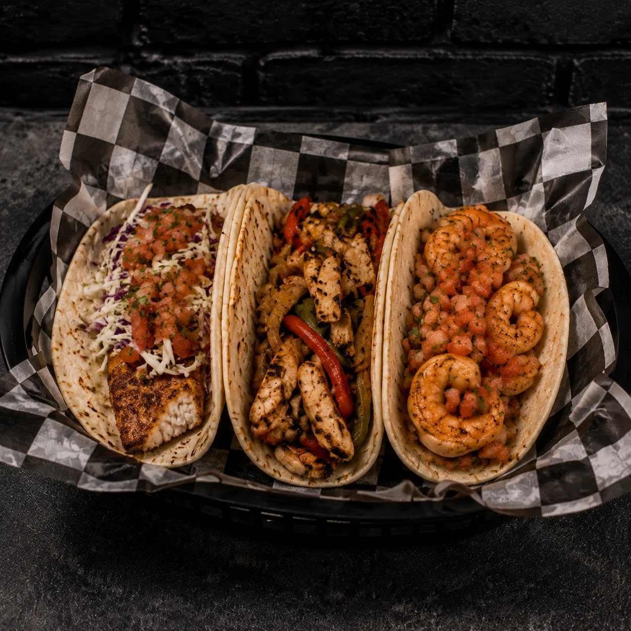 Three delicious tacos featuring fish, chicken, and shrimp on a checkered platter