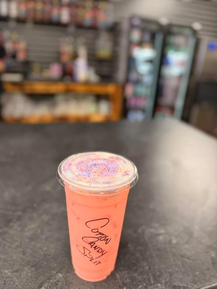 A vibrant pink drink topped with colorful sprinkles in a clear cup, sitting on a black countertop.