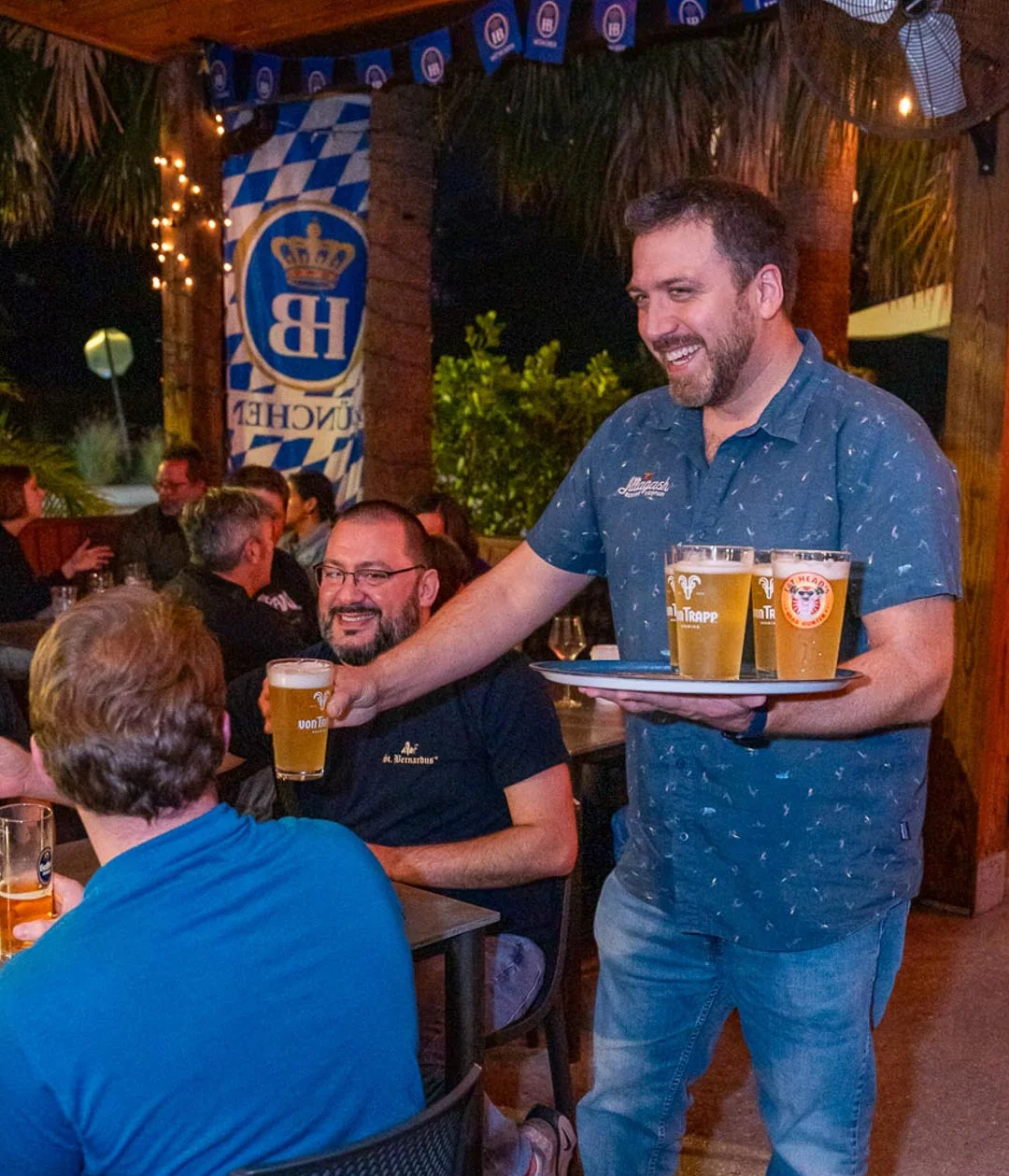 Server delivering drinks to guests in a lively outdoor restaurant setting