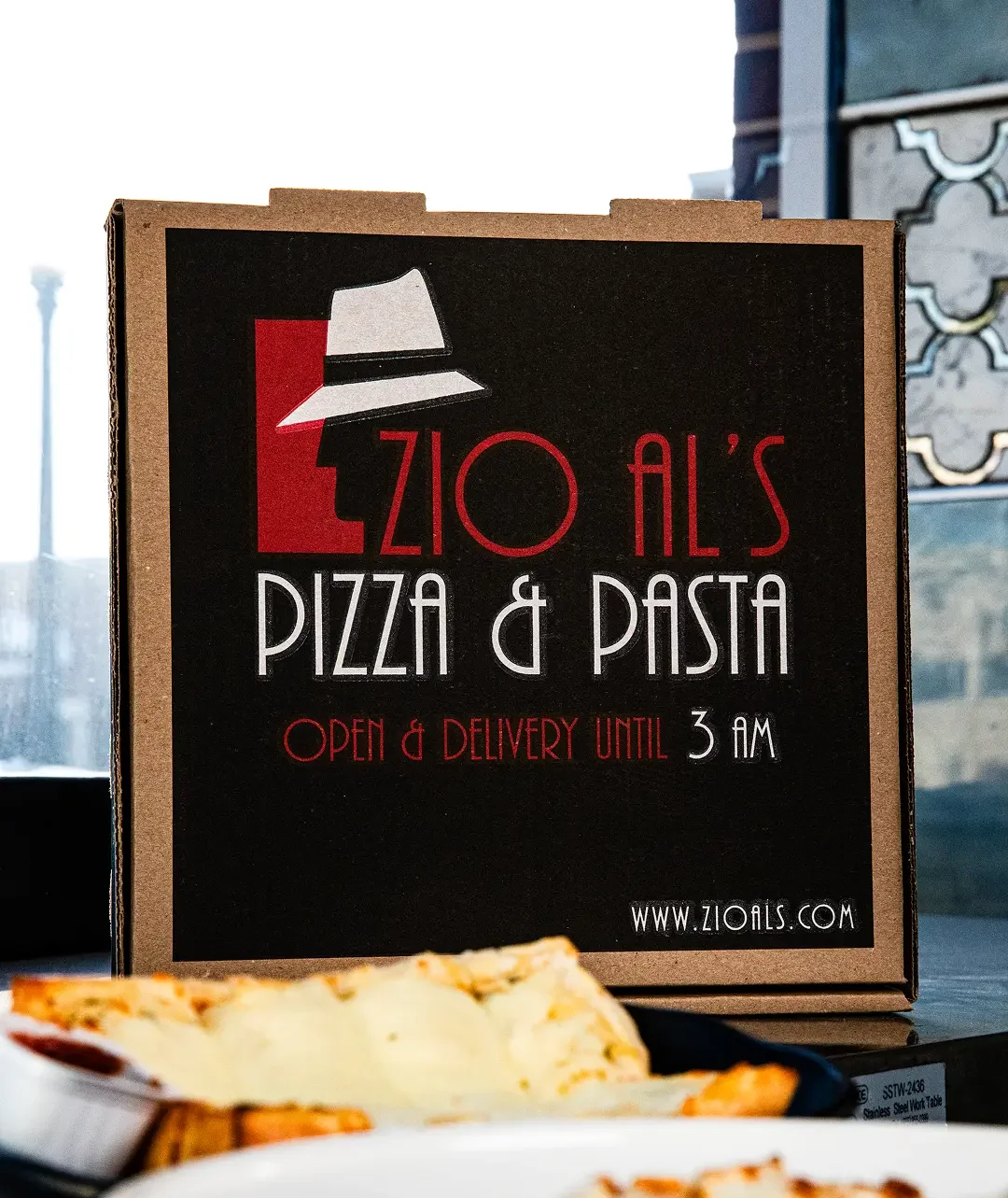 Zio Al's Pizza & Pasta delivery box with food items on a table.
