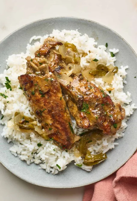 Grilled meat served over a bed of fluffy white rice, topped with sautéed onions and green peppers.
