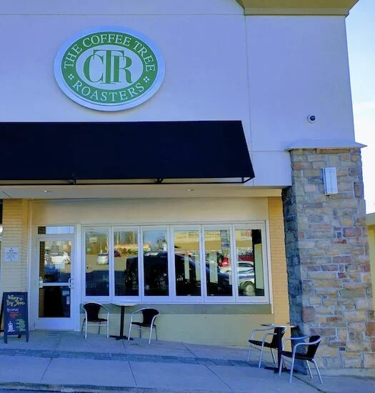 Storefront with a green sign reading "The Coffee Tree Roasters"; a black awning, and large windows reflecting parked cars.