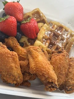 A delicious meal featuring crispy fried chicken wings, fresh strawberries, and waffles topped with syrup and powdered sugar.