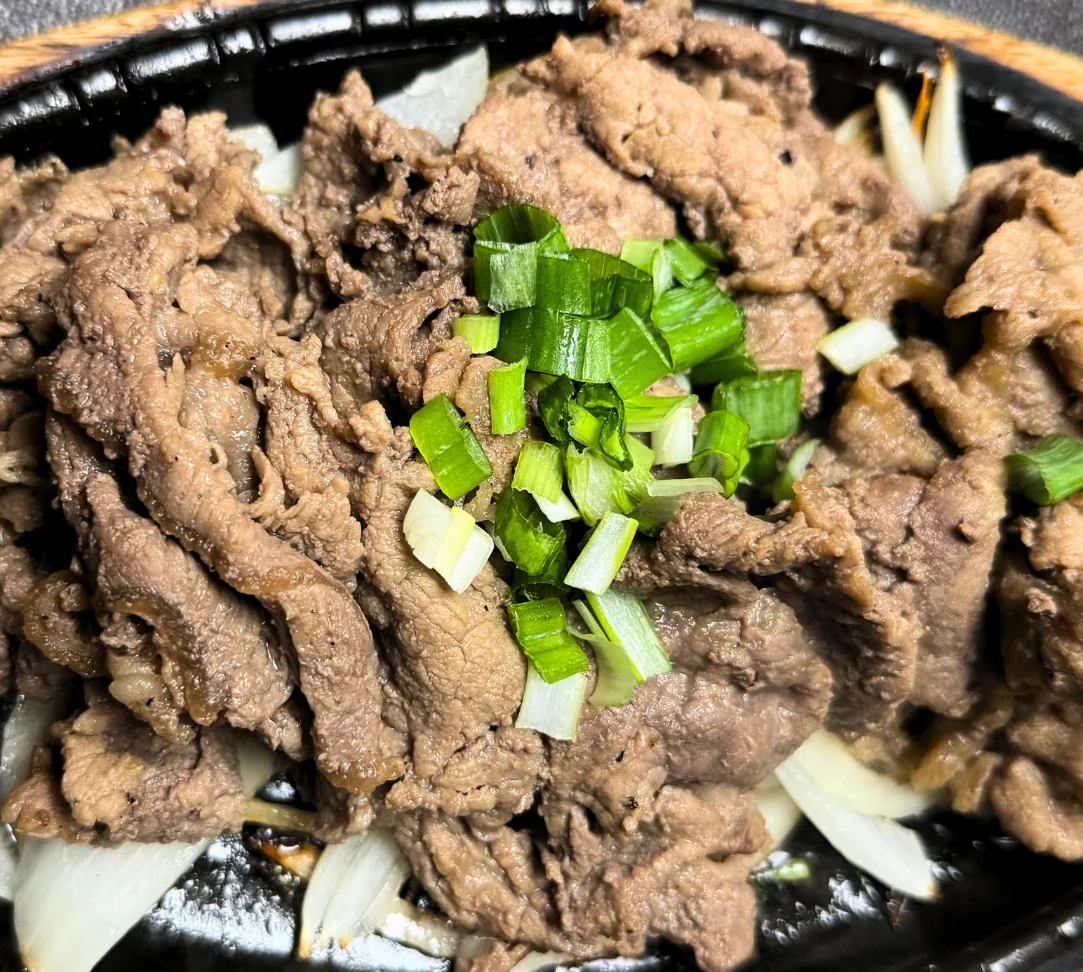 Sizzling beef dish topped with green onions on a black plate.