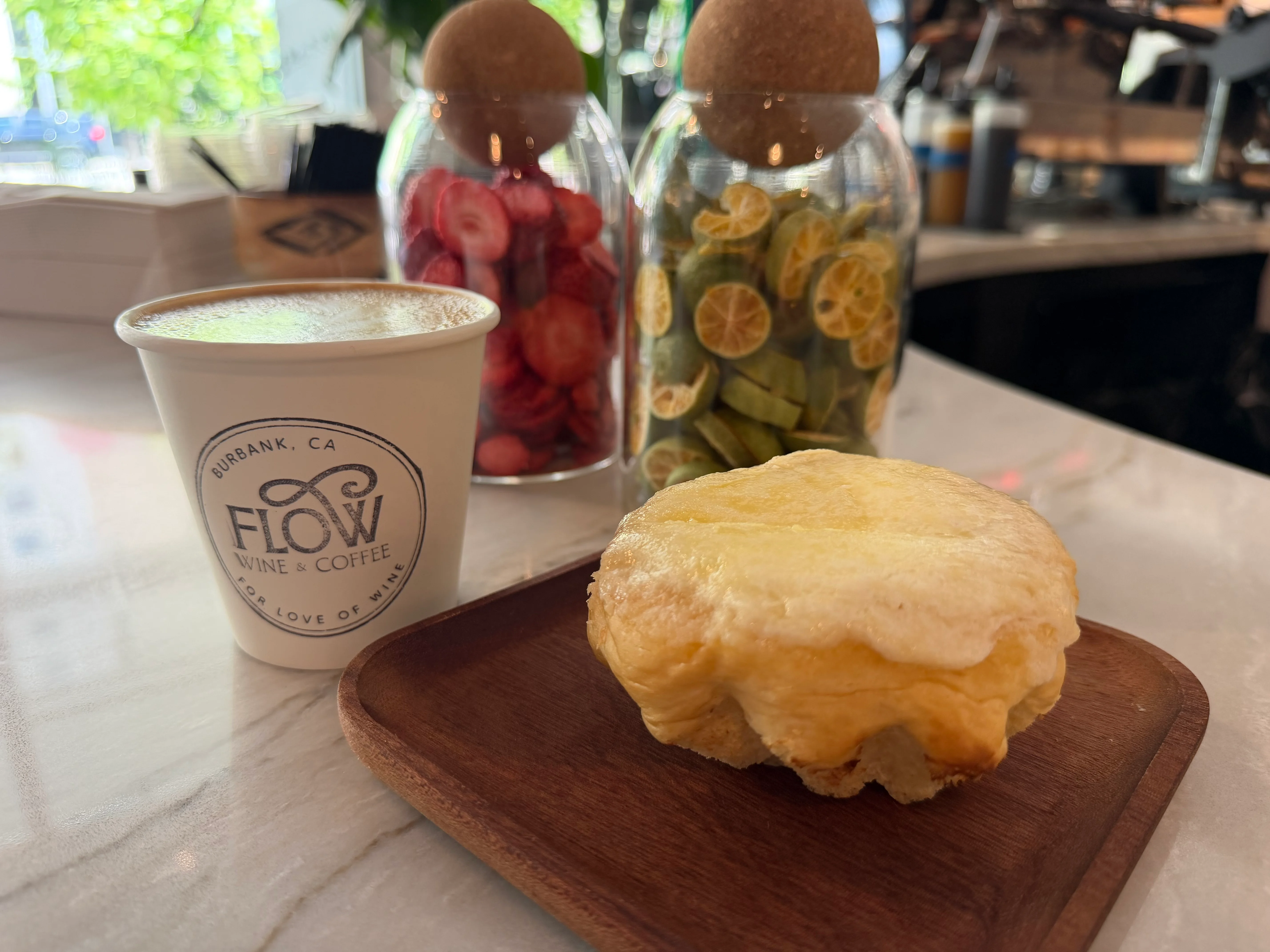 Coffee cup and pastry on a wooden plate with decorative jars in the background.