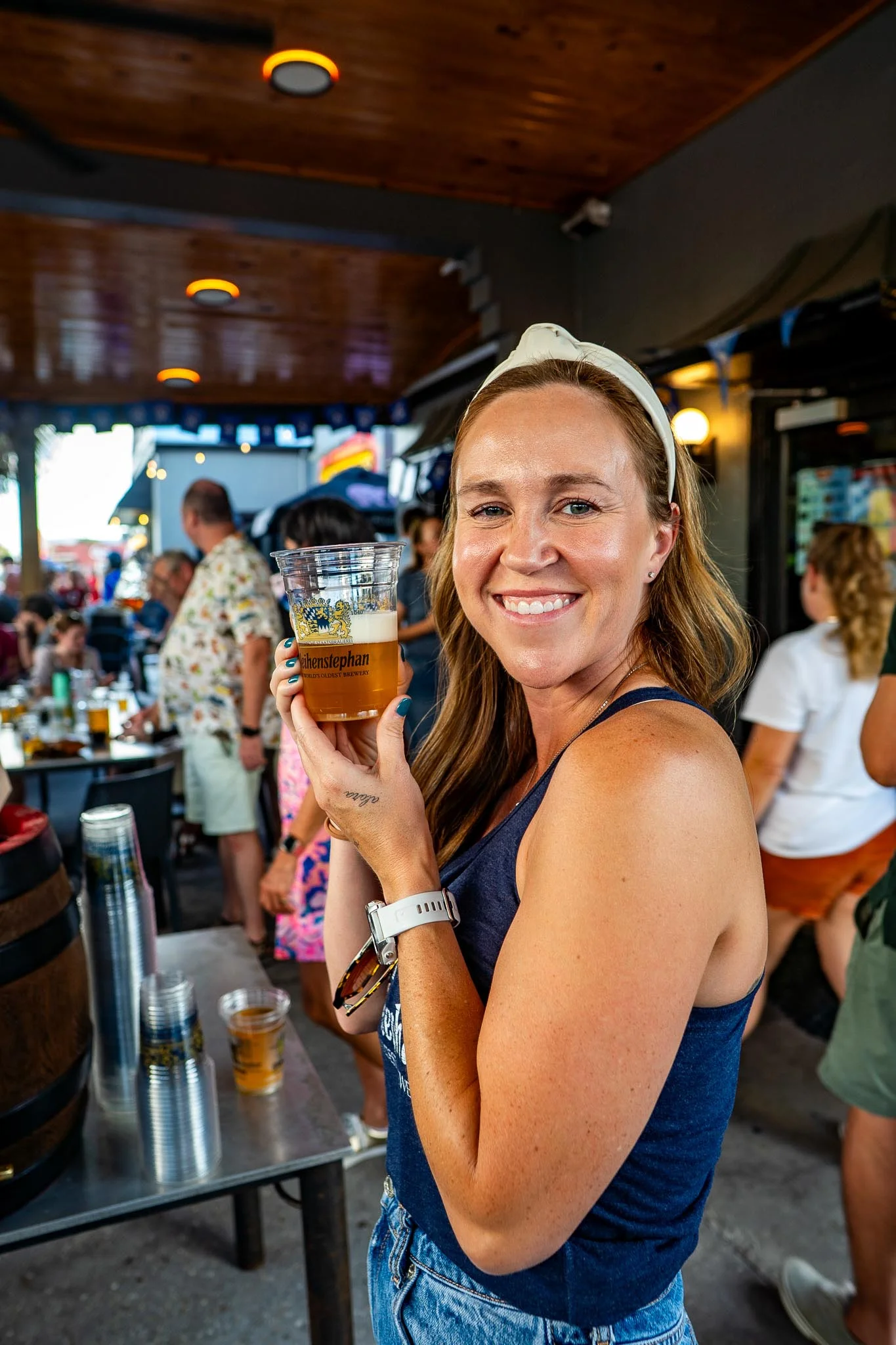 Smiling woman holding a beer at a lively outdoor bar