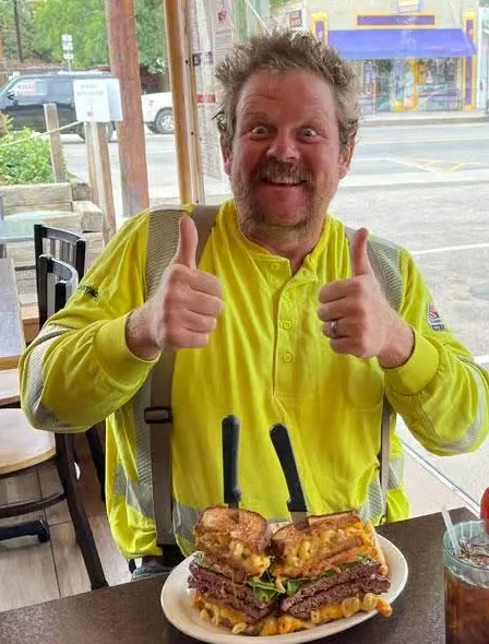 Man enjoying a towering burger platter in a cozy diner