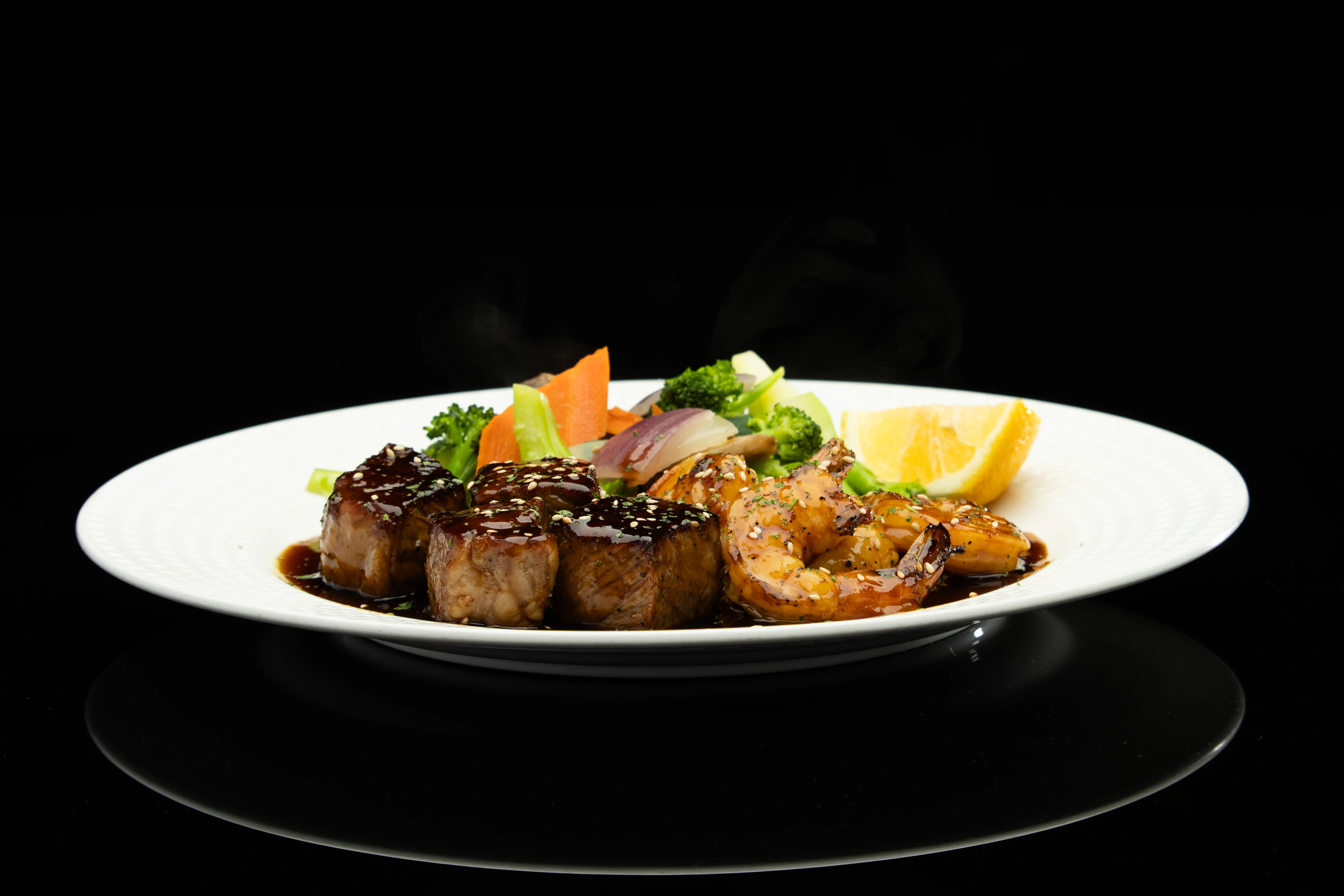Grilled shrimp and steak teriyaki with vegetables on a white plate