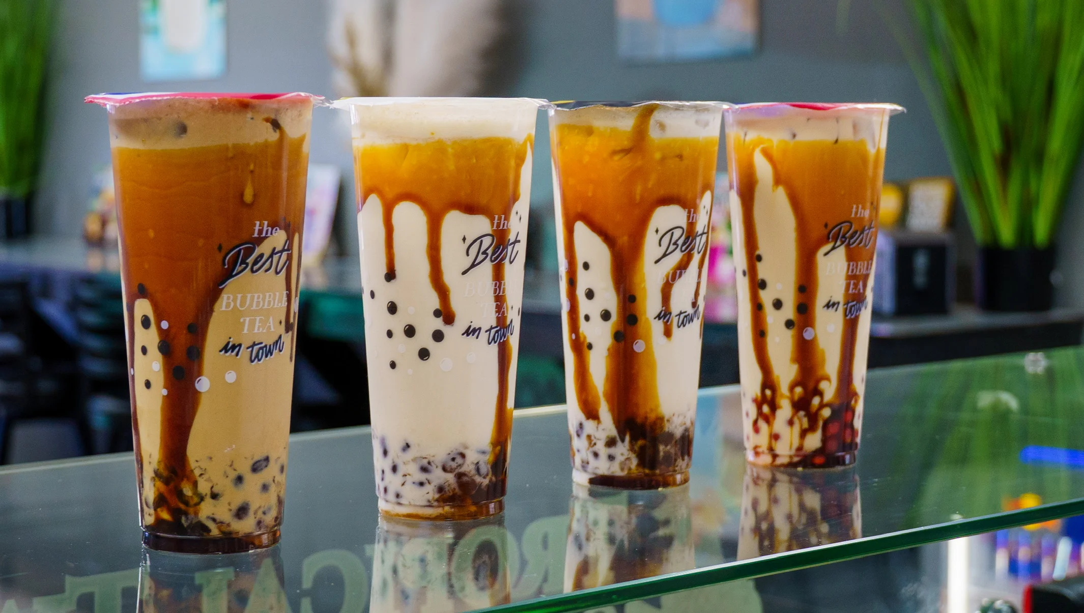 Four colorful bubble tea drinks with tapioca pearls on a counter.