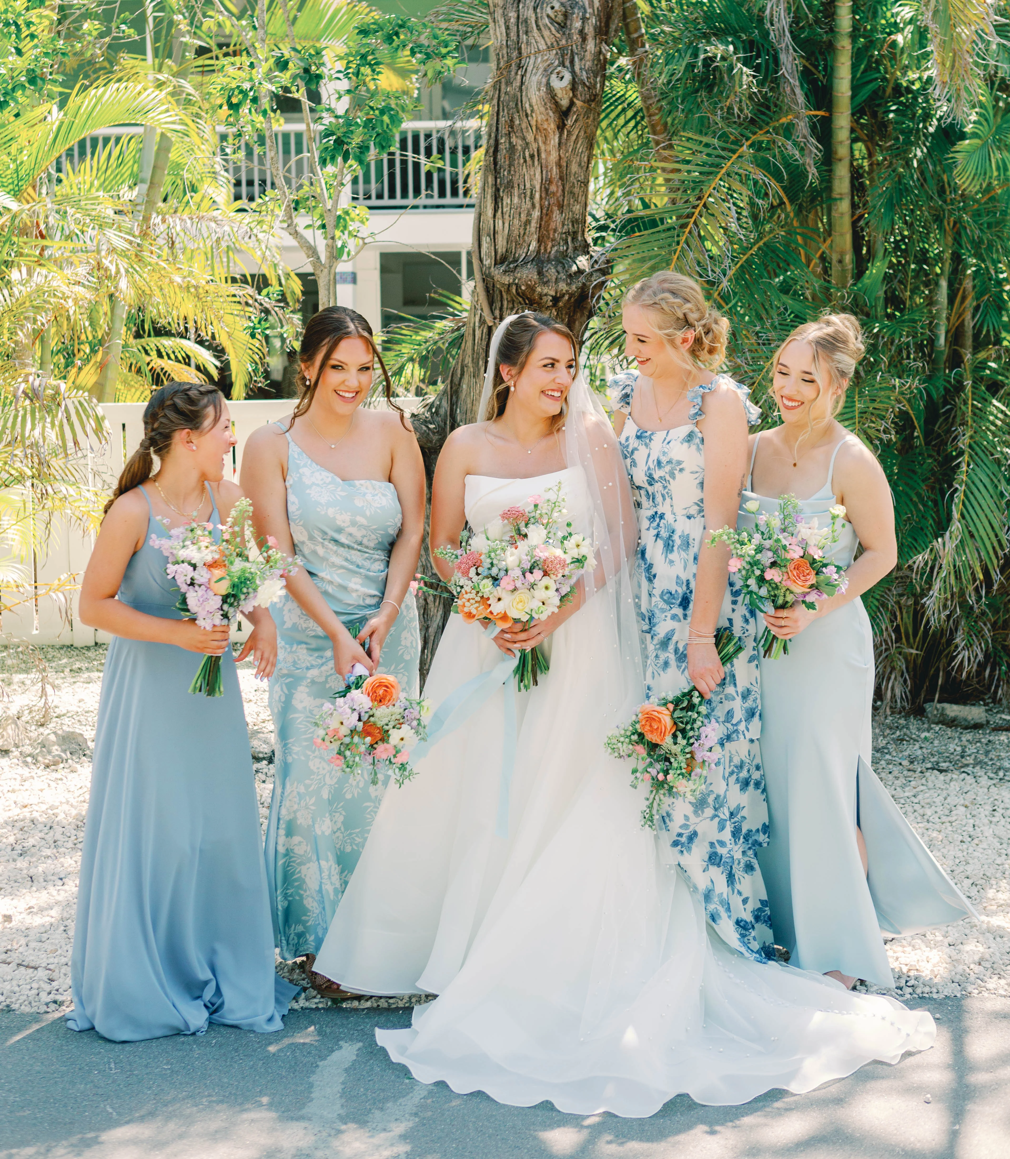 Bridesmaids in elegant dresses with floral bouquets in a tropical setting