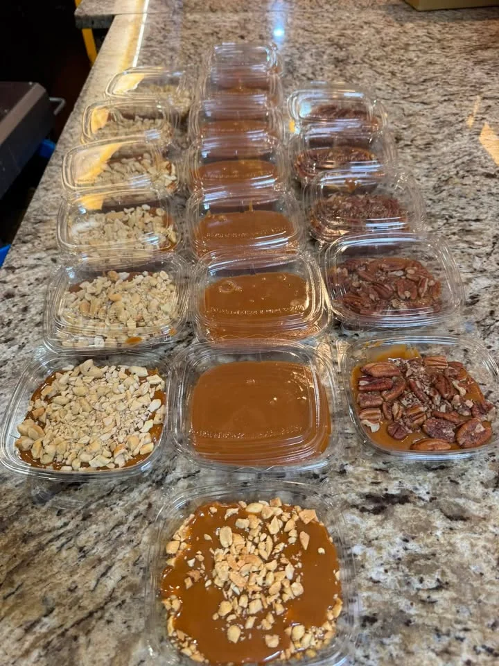 An organized array of caramel dessert cups on a countertop, each topped with different nut varieties and arranged in precise rows.