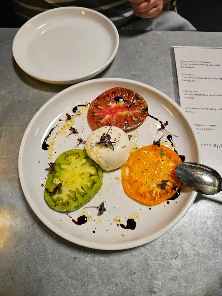 A plate with three colorful heirloom tomato slices, served with a dollop of creamy cheese and drizzled with balsamic.