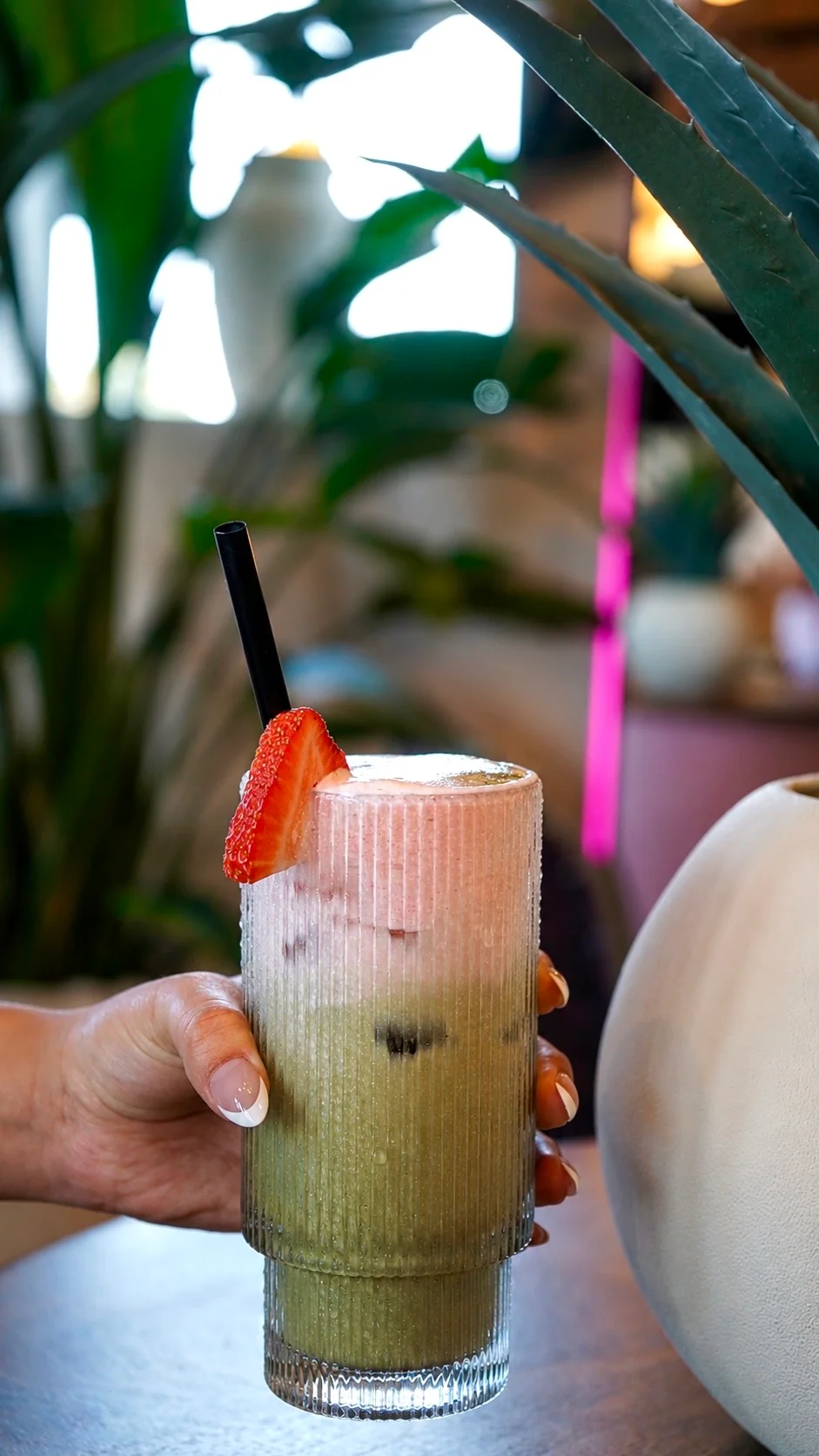 A elegantly presented cocktail in a coupe glass, topped with a vibrant orange flower, against a blurred bar backdrop.