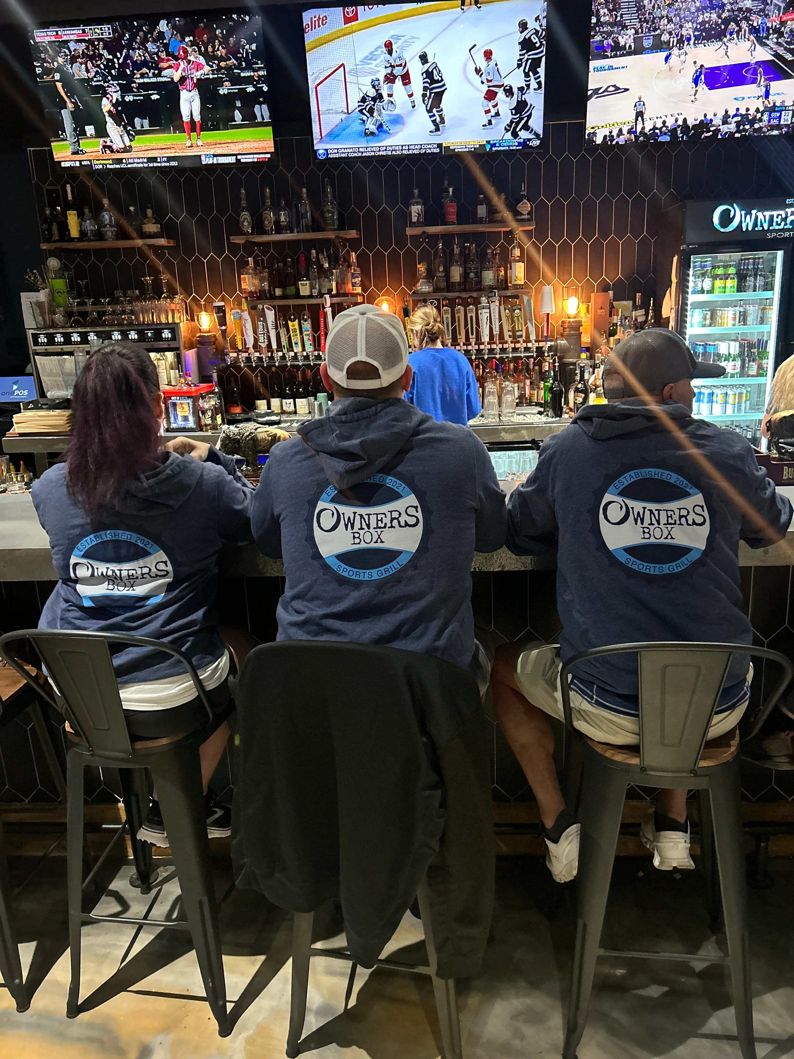 Bartenders at a sports grill with multiple screens showing live games