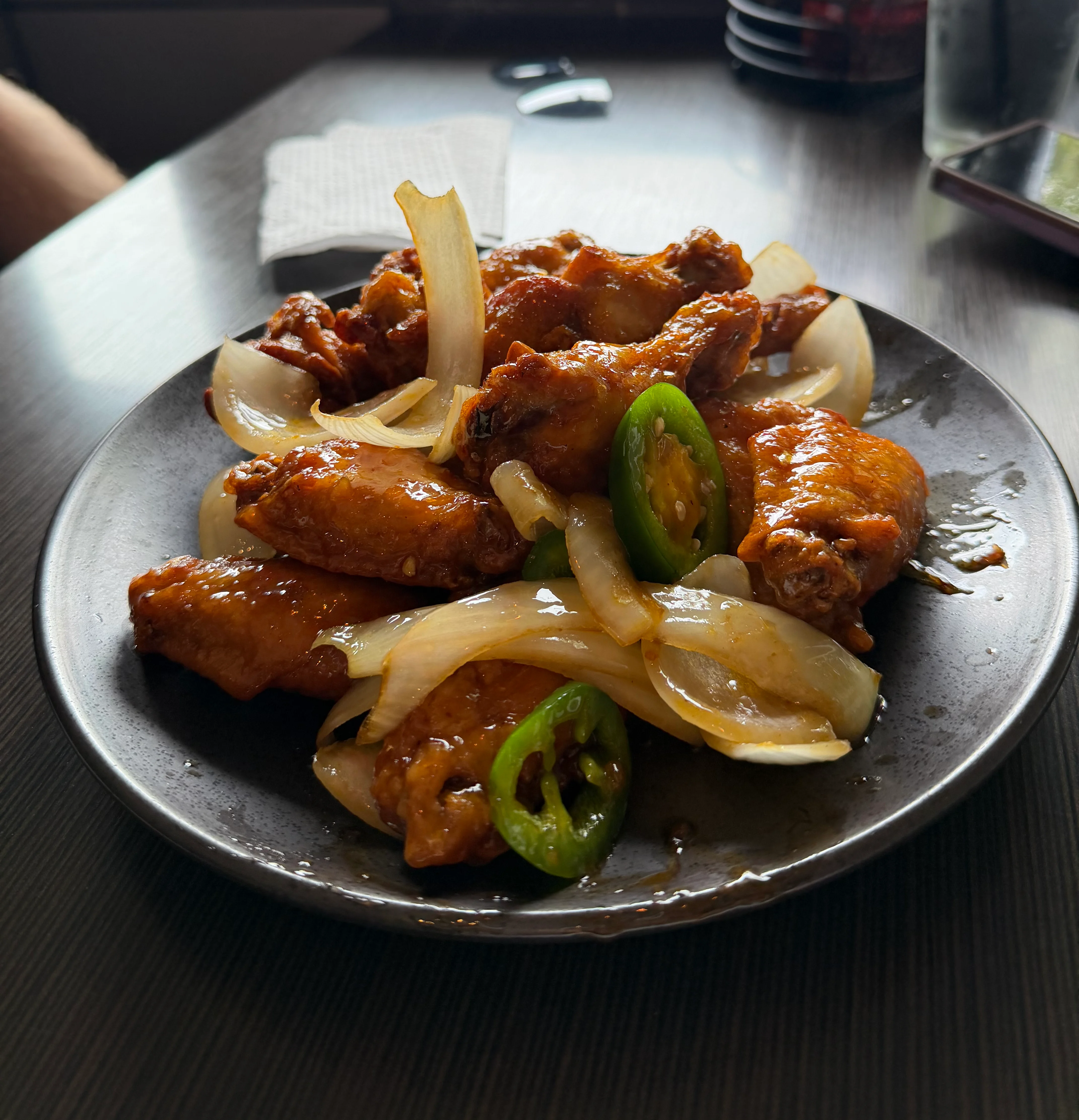 Spicy Korean fried chicken with onions and jalapeños on a black plate