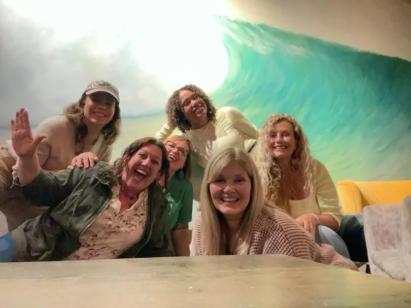 A cheerful group of friends posing together in front of a colorful wave mural, showcasing their smiles and playful expressions.