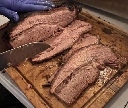 Sliced smoked brisket on a wooden cutting board, showcasing BBQ style