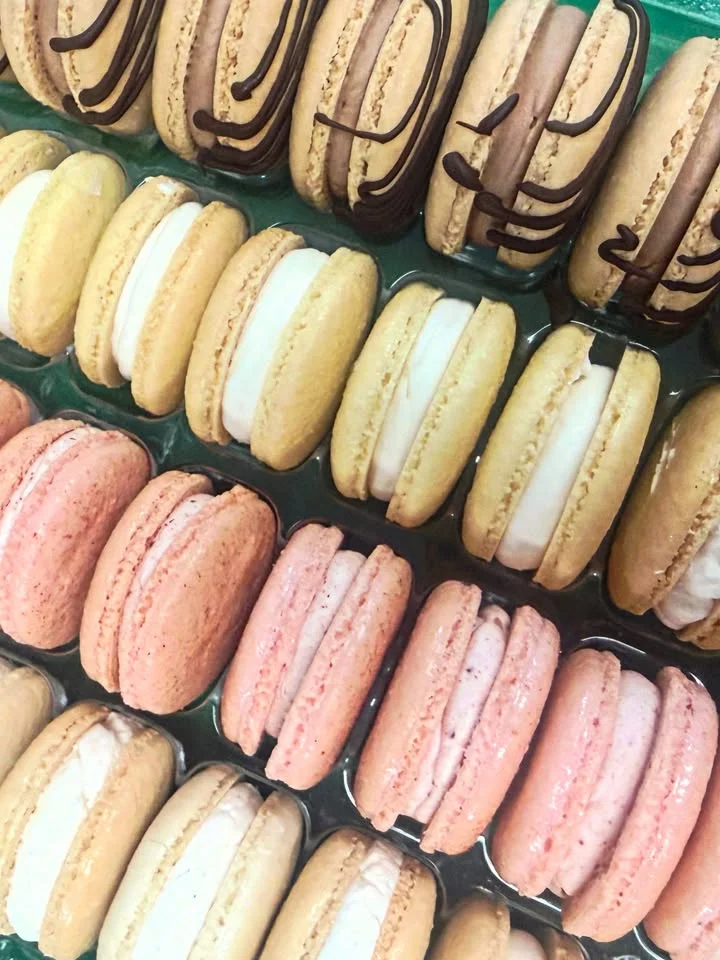 A variety of colorful macarons arranged in a row, featuring flavors such as chocolate, vanilla, and strawberry.