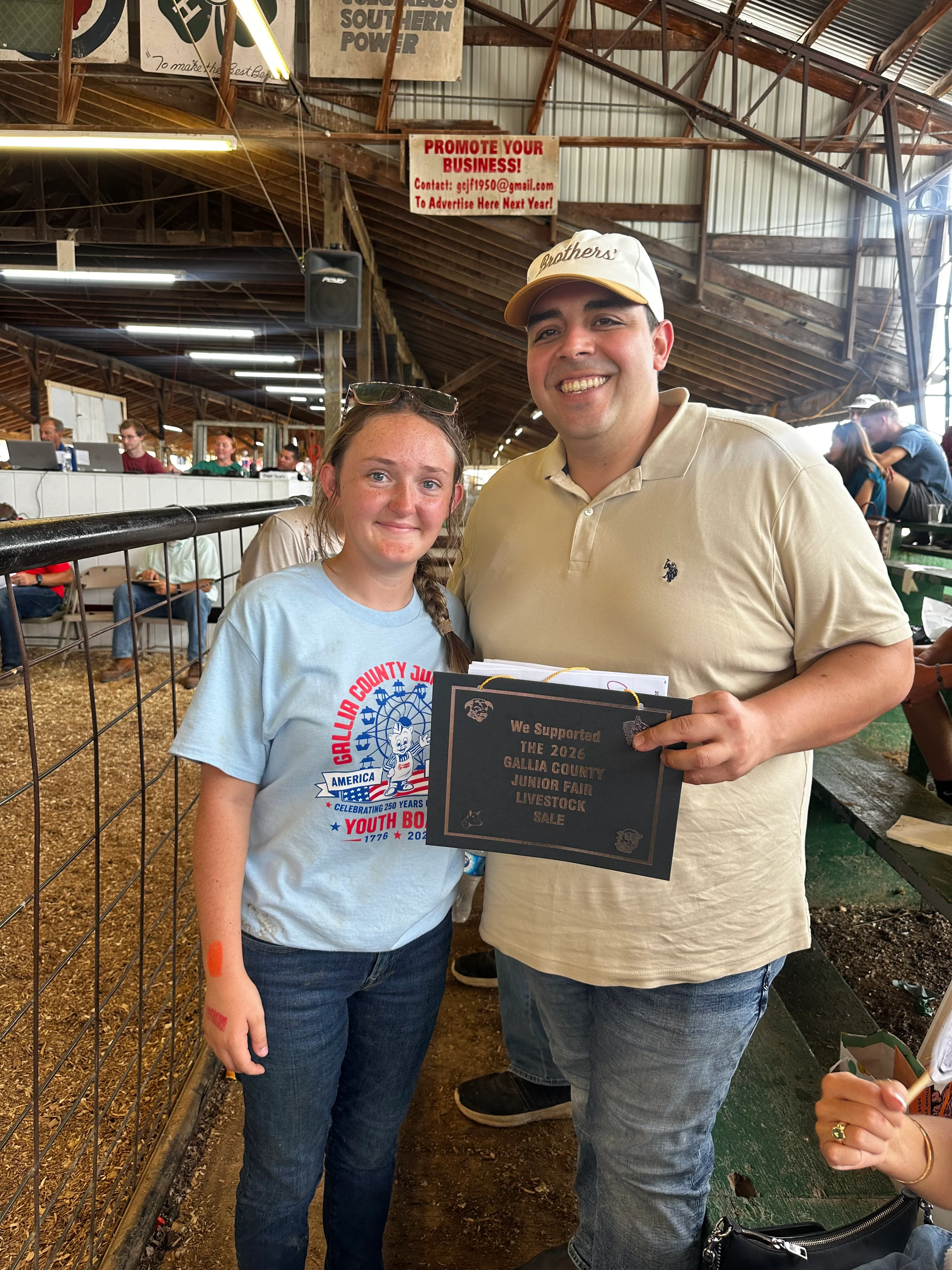 Two young people at a livestock sale event holding a support plaque