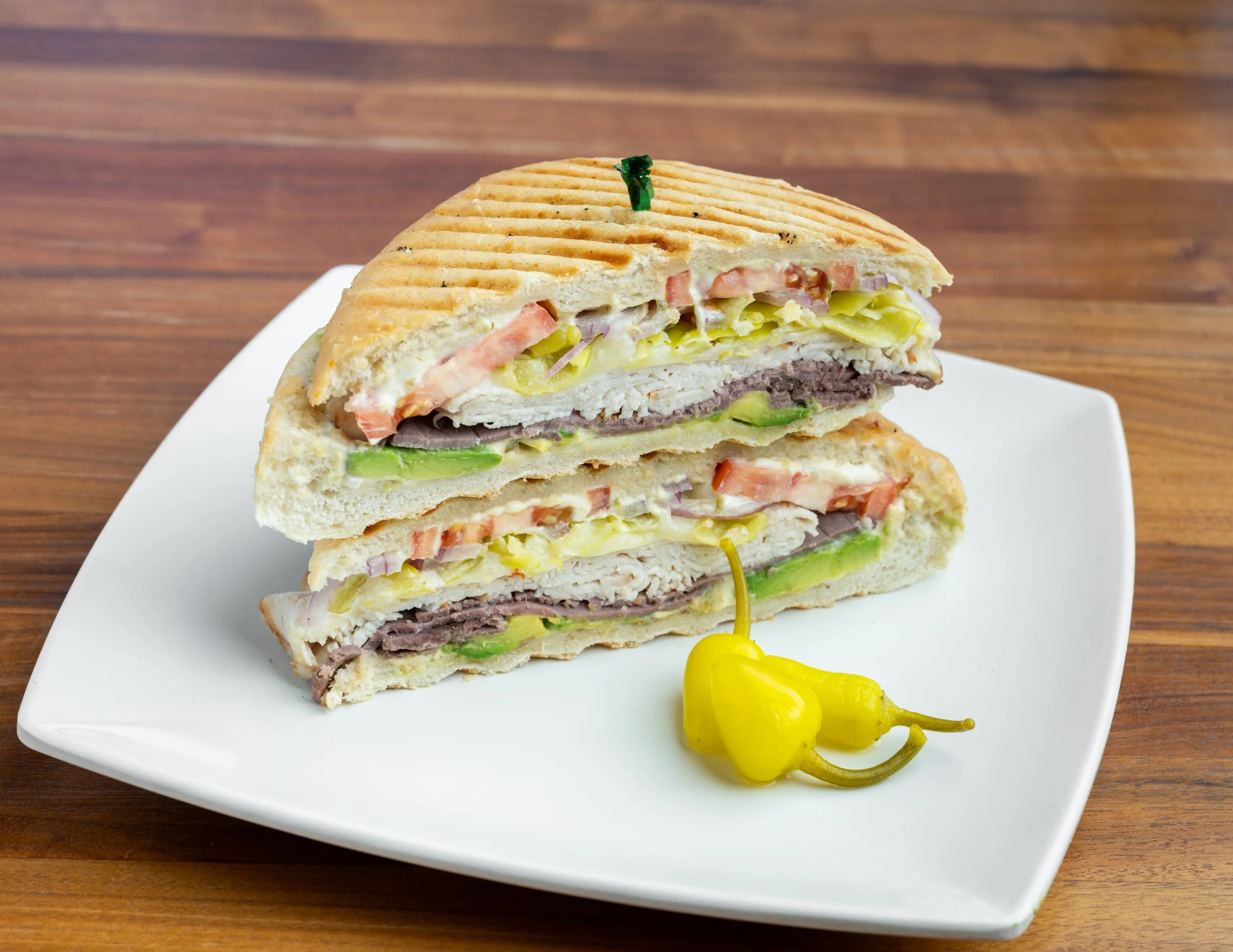 Panini sandwich with roast beef, avocado, tomato, pepperoncini