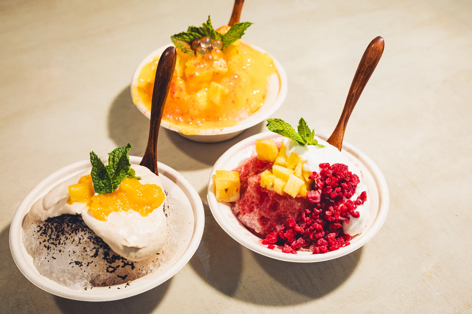 Three bowls of hand-shaved Hawaiian shave ice with mango, coconut cream and strawberry toppings.