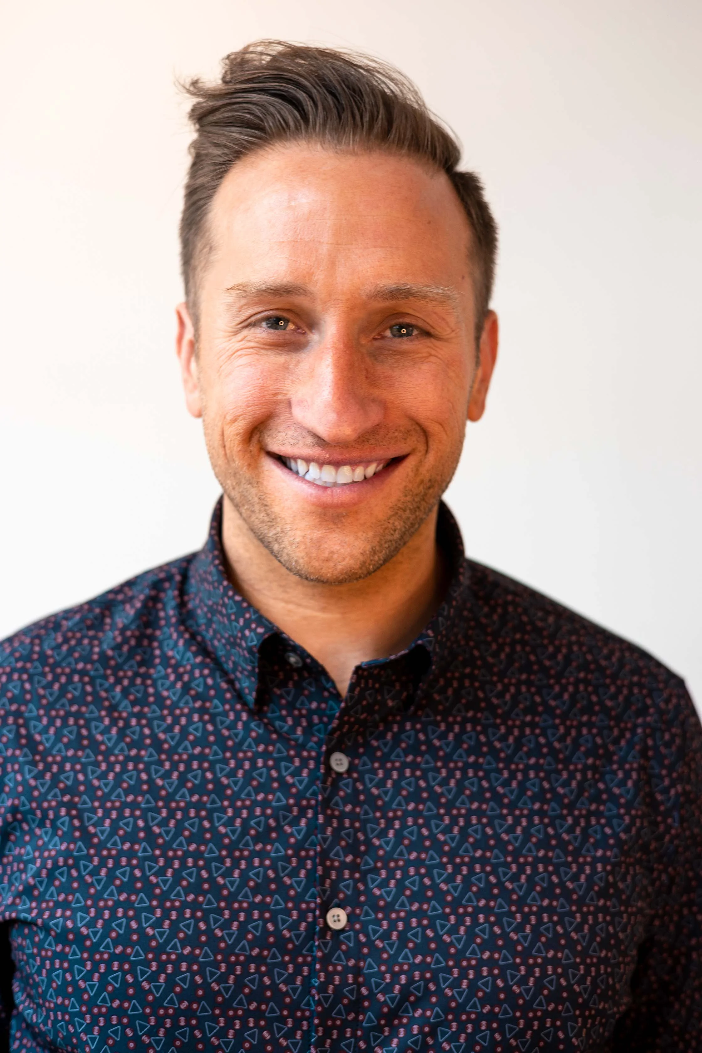 Smiling man in a patterned shirt against a neutral background