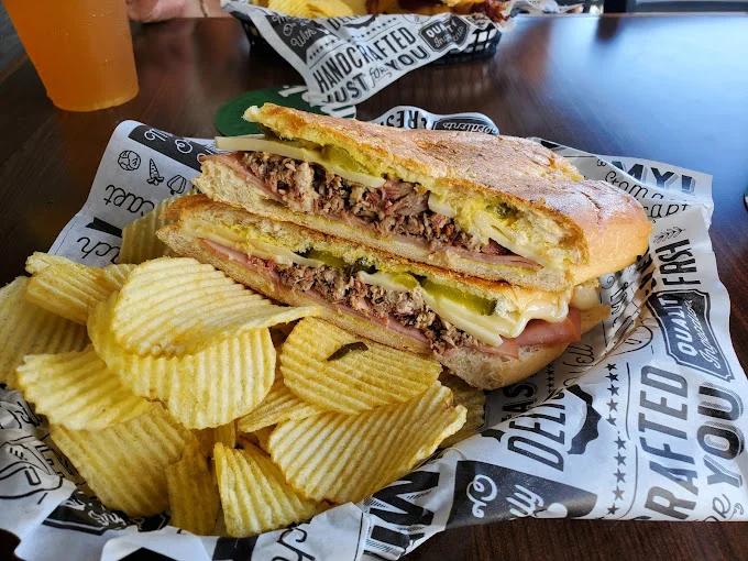 A sandwich filled with layers of meats, cheese, and pickles, accompanied by a side of ridged potato chips.
