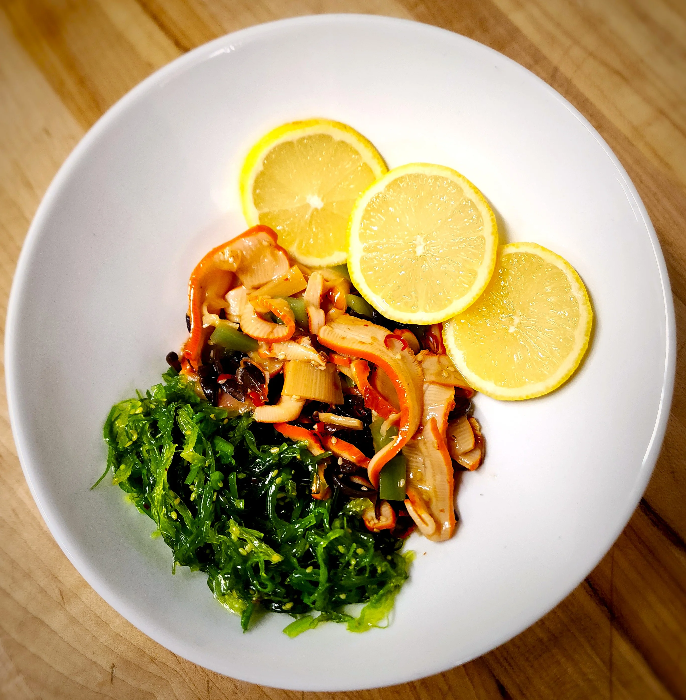 Colorful dish with vegetables, seaweed, and lemon slices in a white bowl.