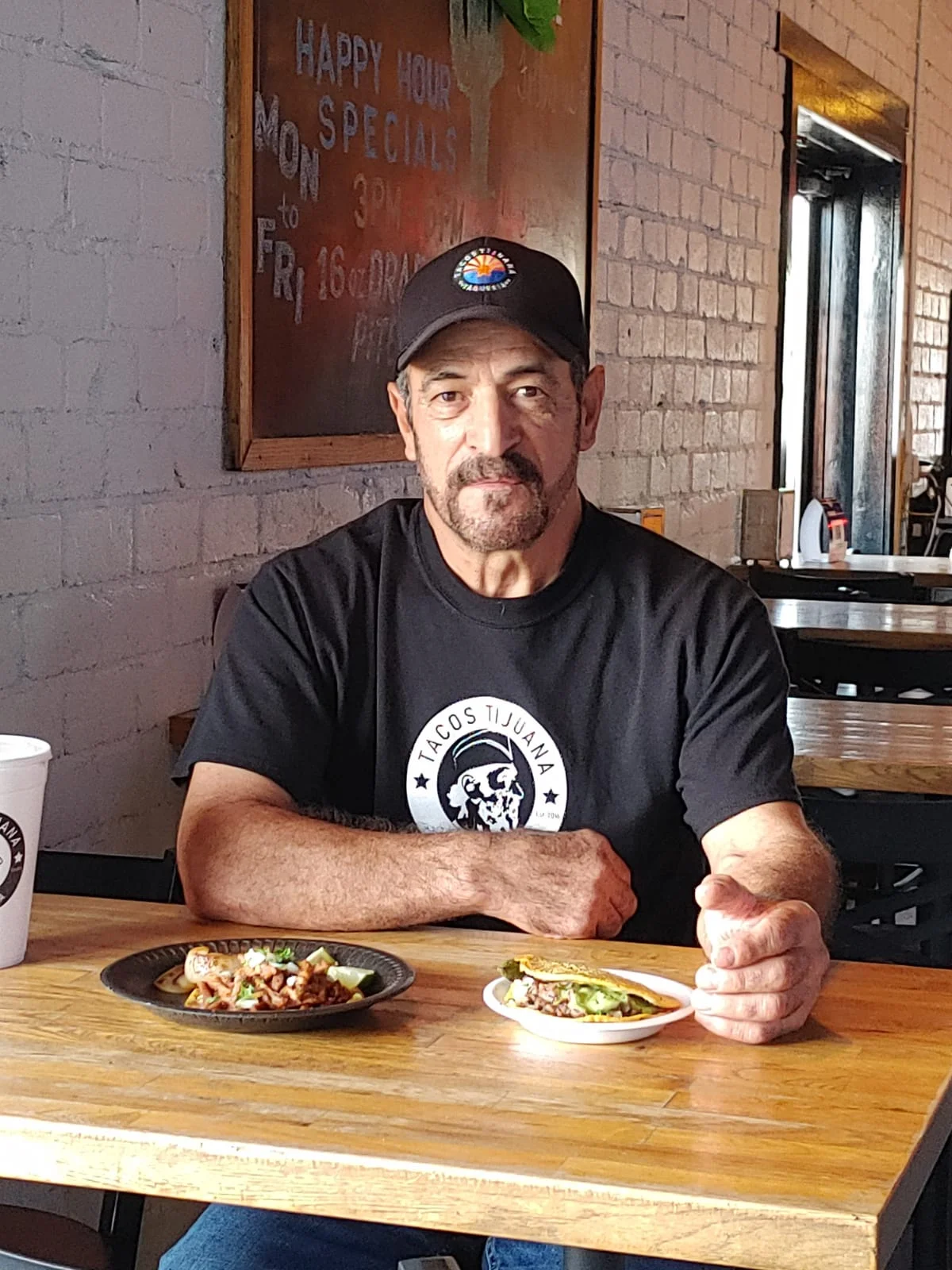 The owner of Tacos Tijuana sitting comfortably in his restaurant with a plate of signature dishes on the table