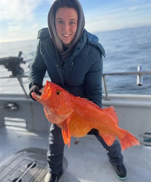 Angler proudly holding a large orange rockfish on a boat
