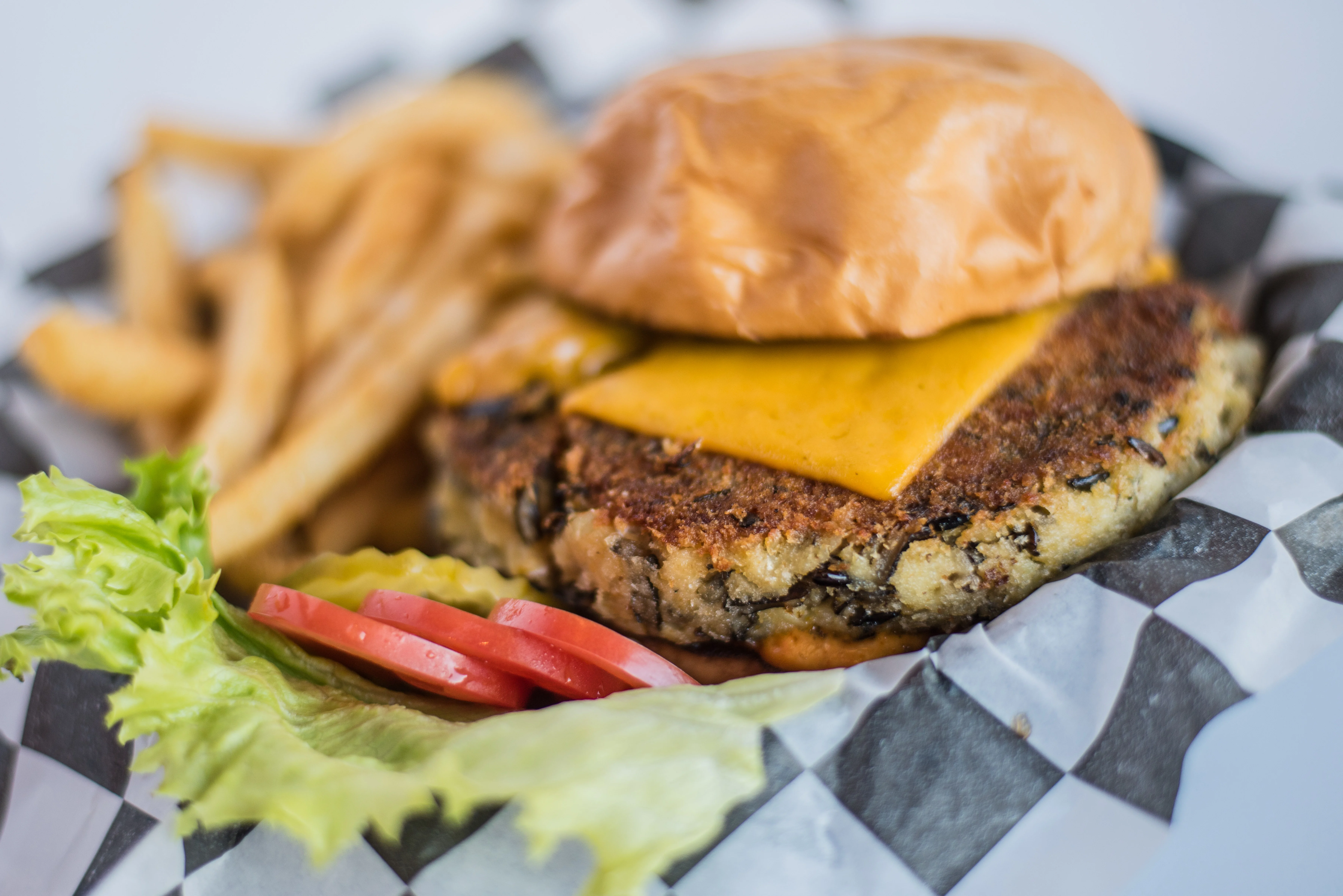 A burger with a veggie patty topped with melted cheese, served with a side of fries and fresh lettuce and tomato.
