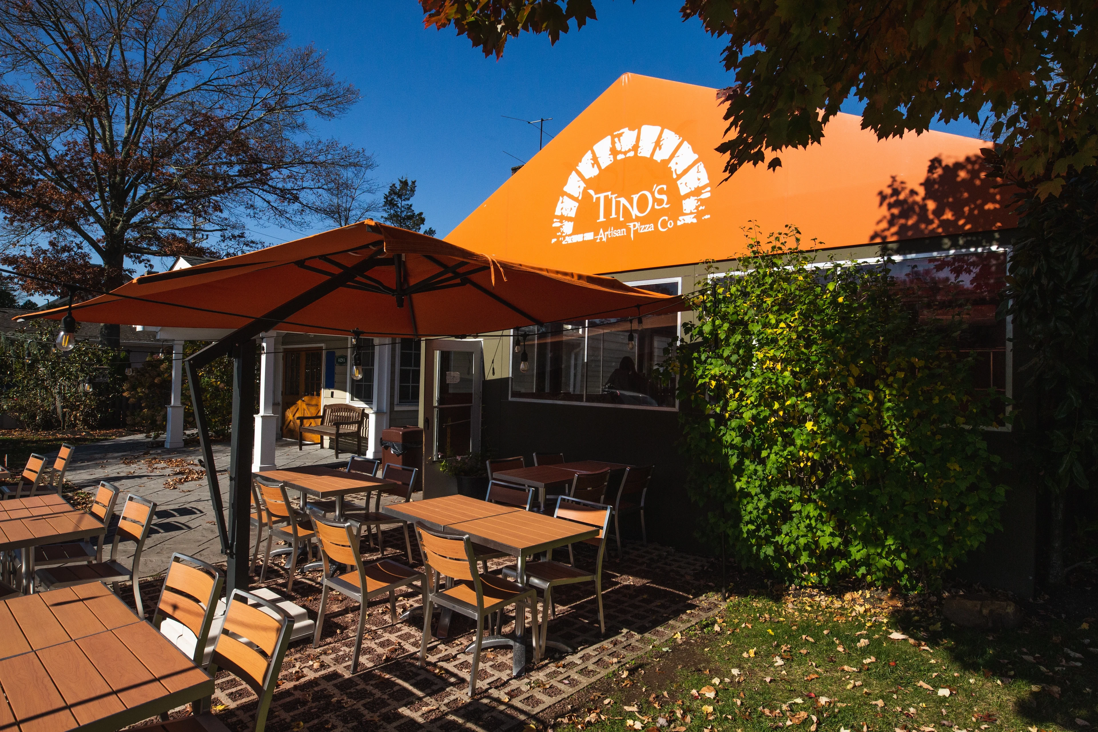 Outdoor dining area of Tino's Artisan Pizza Co with orange umbrellas