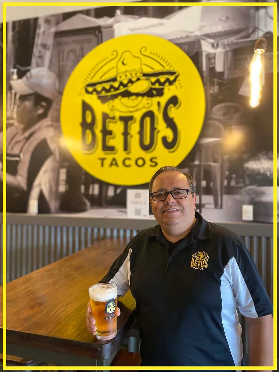 Owner of Beto's Tacos holding a beer in a vibrant restaurant setting