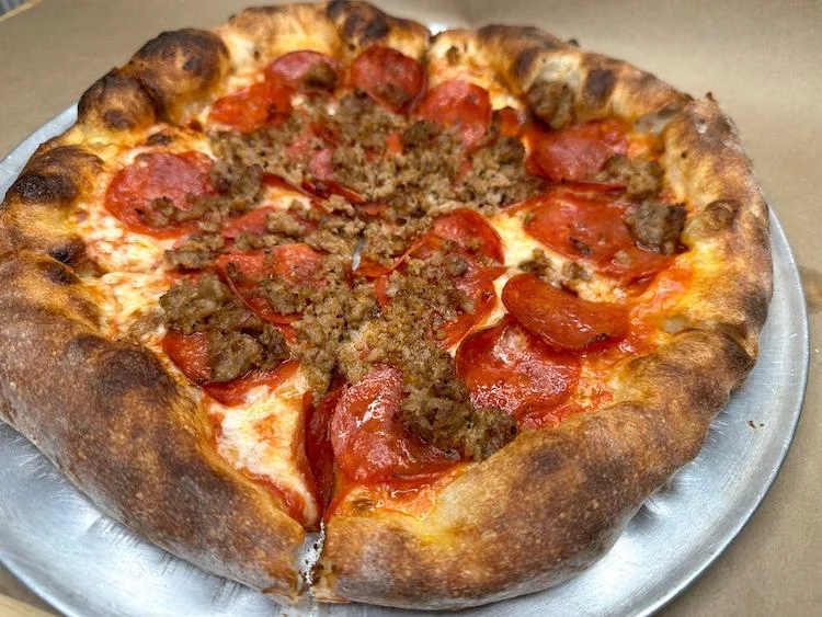 A large pizza featuring a crispy crust topped with pepperoni and sausage, served on a metal plate.