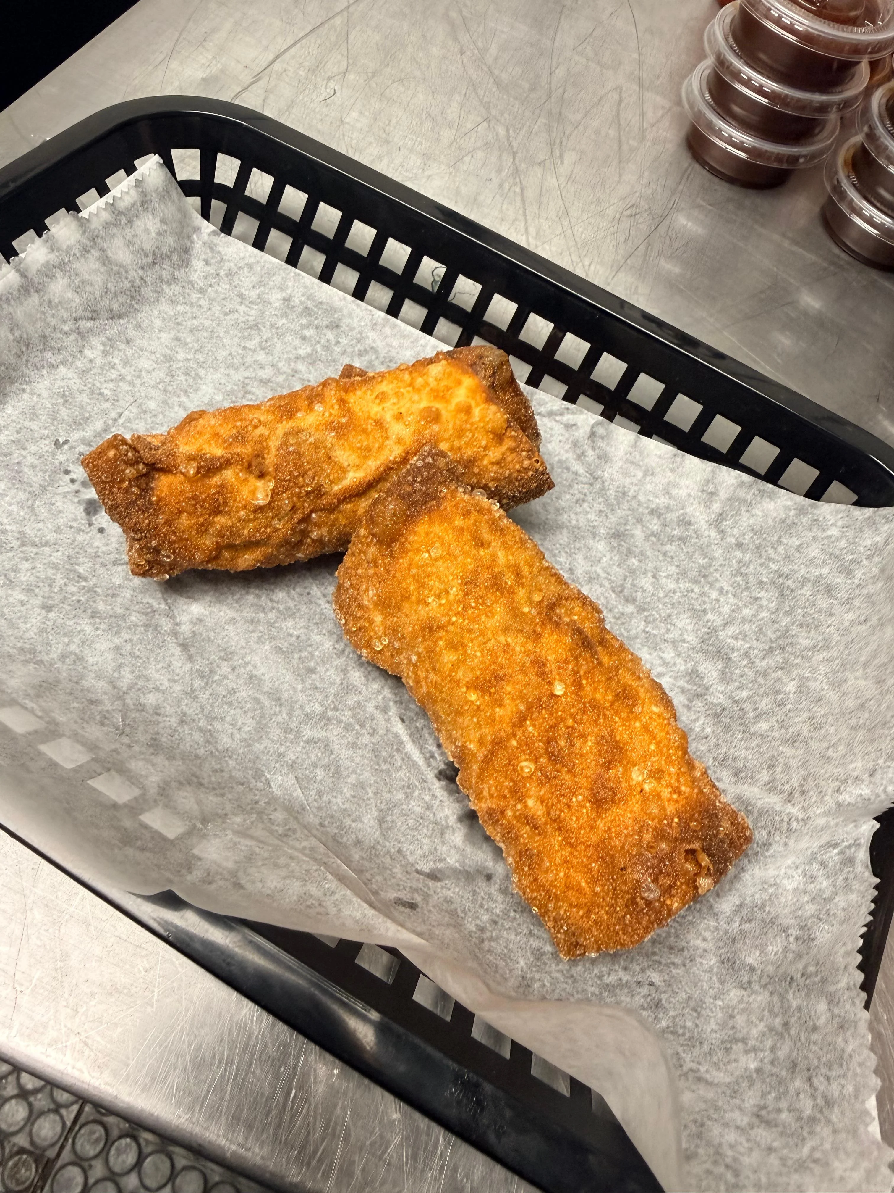 Two crispy fried egg rolls on a serving tray with parchment paper.