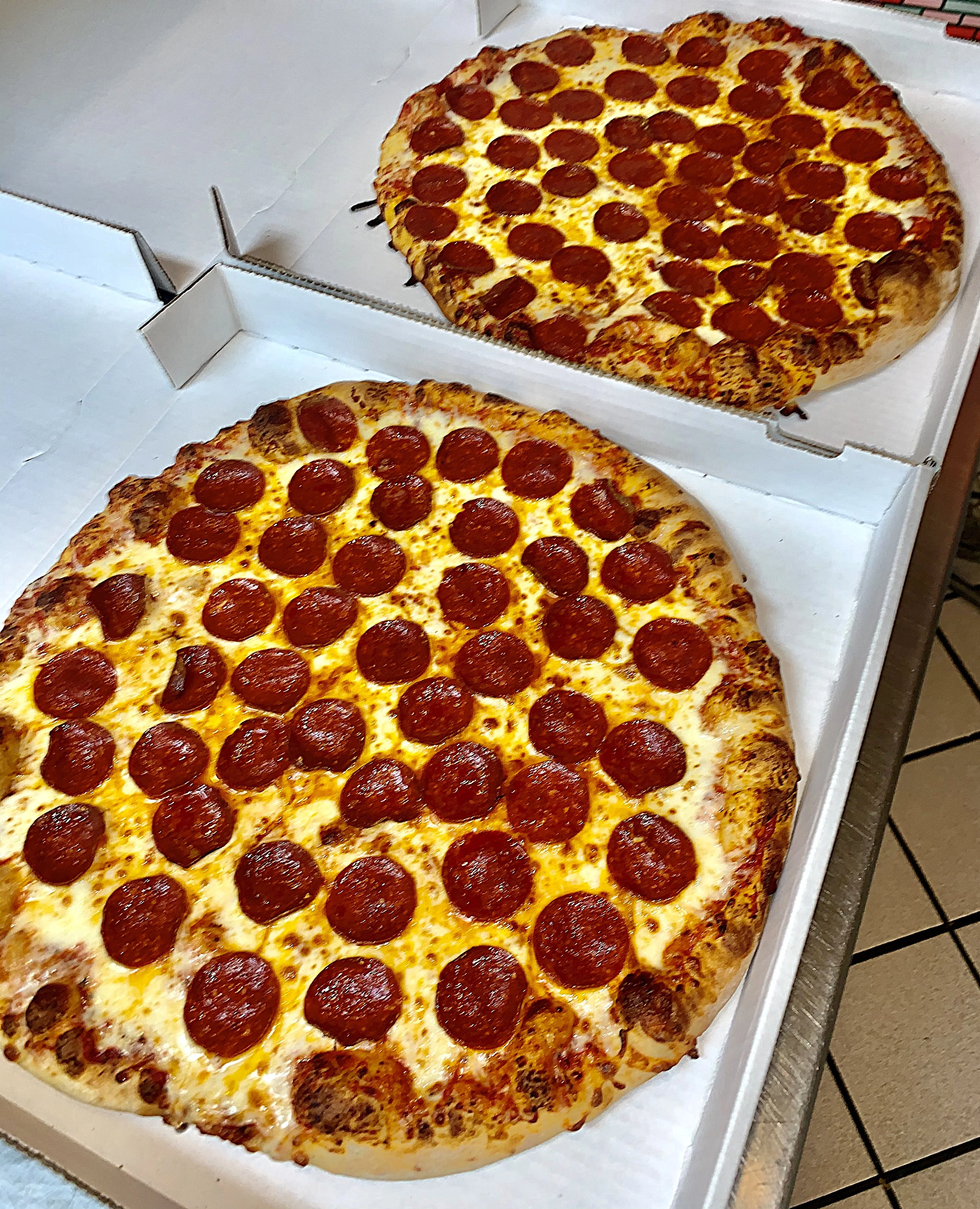 Two large pizzas with a golden crust, topped generously with slices of pepperoni, placed in open pizza boxes.