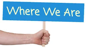 Hand holding a blue sign that says 'Where We Are'