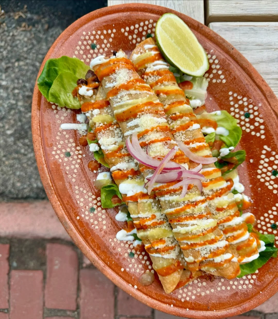 Crispy Mexican flautas drizzled with sauce and garnished with lime
