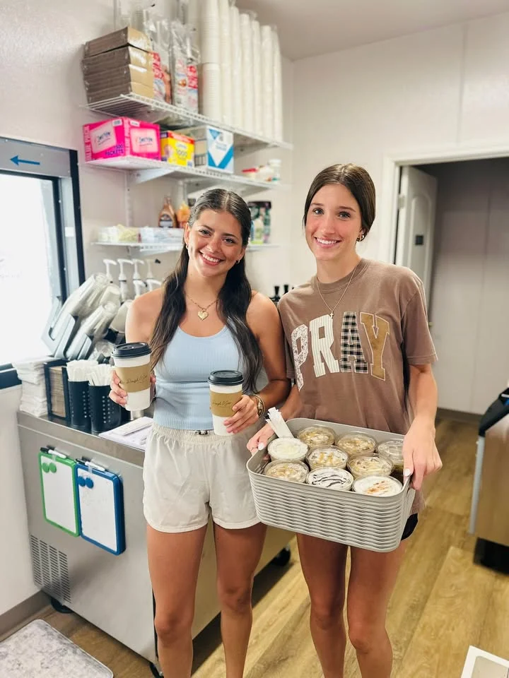 Two women in a cafe holding coffee and desserts