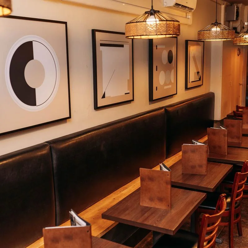 A cozy dining area featuring modern geometric art prints on the wall, with dark seating and wooden tables.