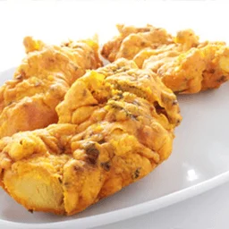 Golden deep-fried Indian vegetable pakoras on a white platter.