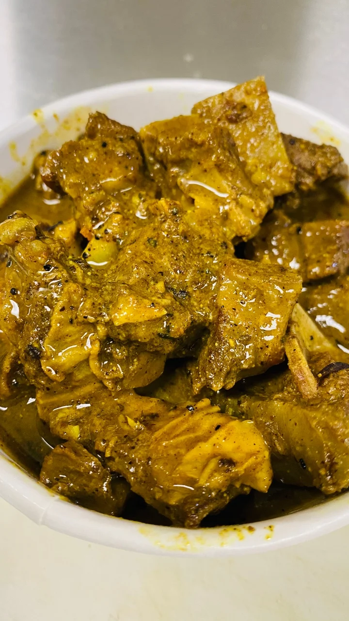 A bowl of tender meat pieces coated in a rich, spiced sauce, with some visible herbs and spices.