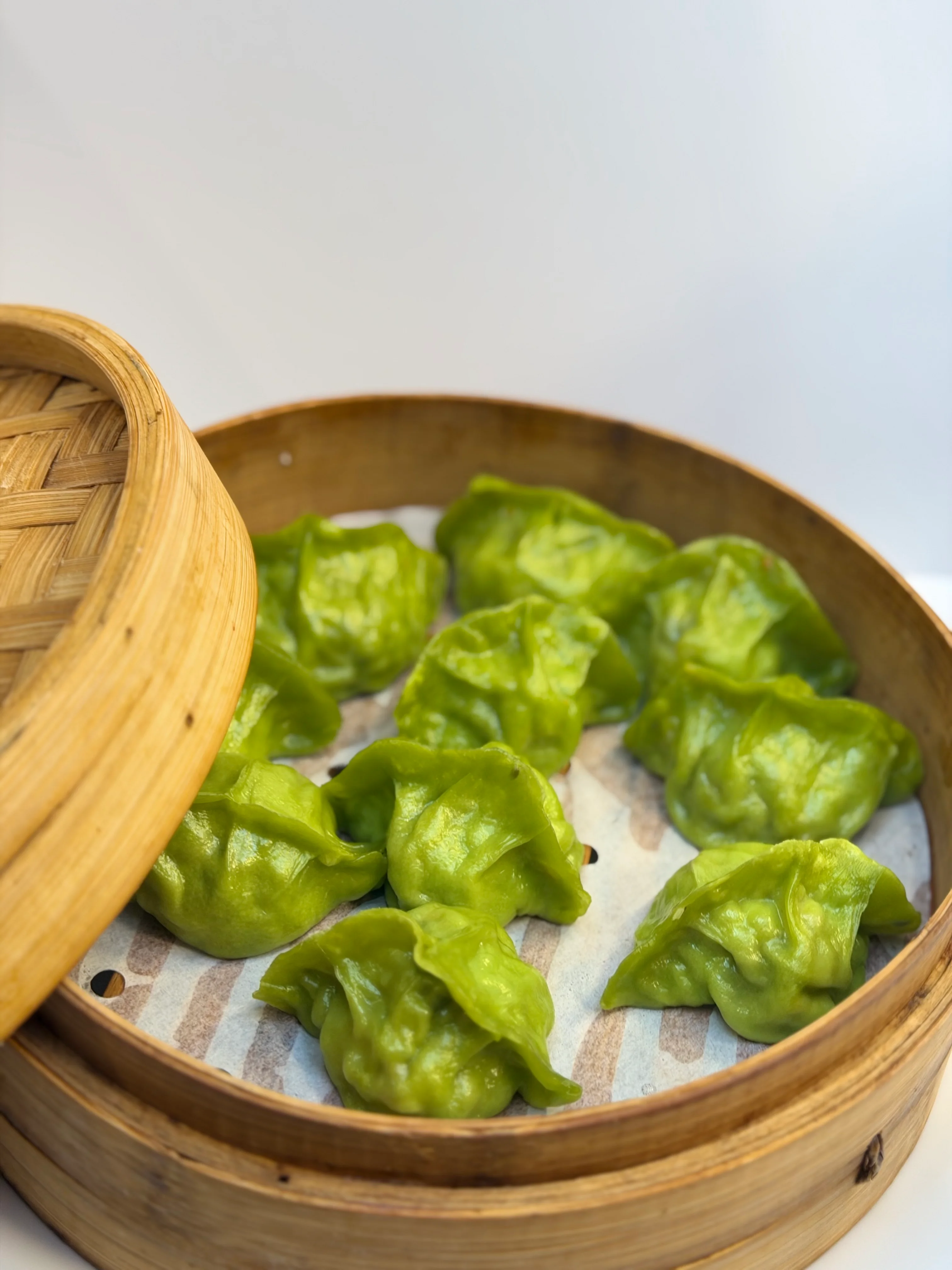 A bamboo steamer containing three fluffy bao buns, each beautifully shaped with a garnish on top, resting on parchment paper.