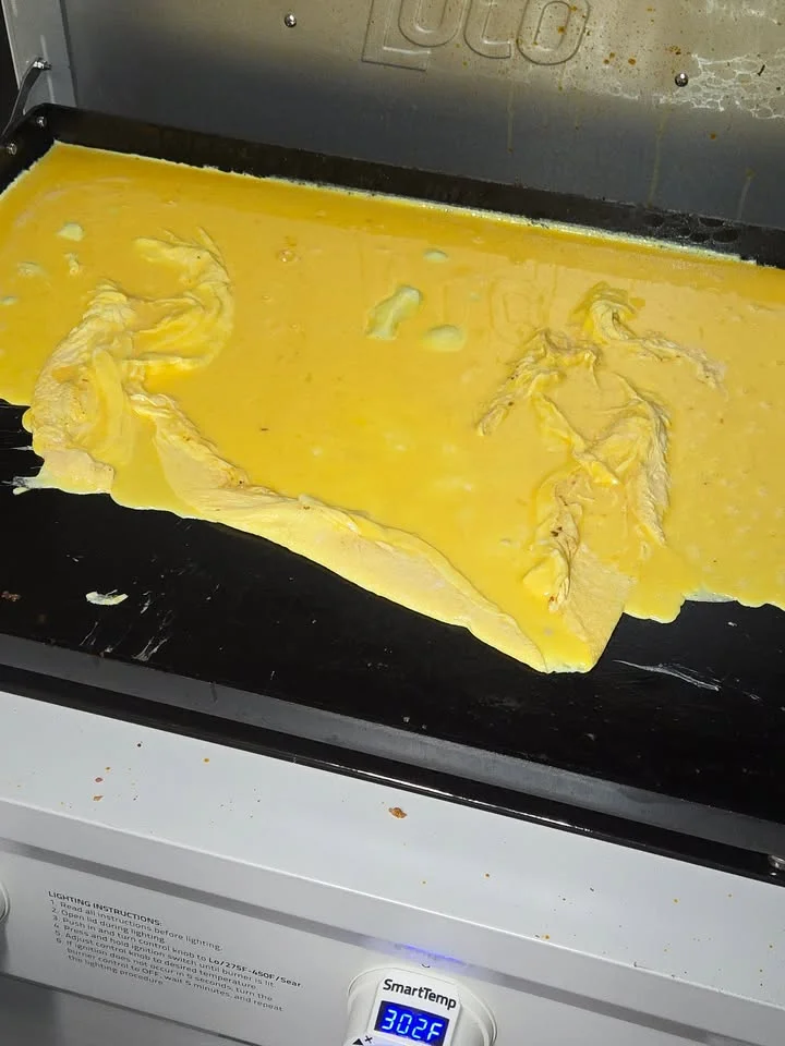 A large flat griddle showing eggs being cooked and prepared, with an adjustable temperature display on the side.