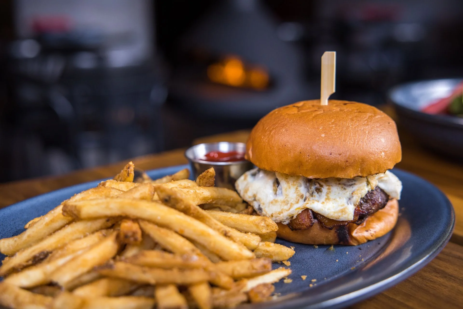 Juicy burger with fried egg and fries on a blue plate