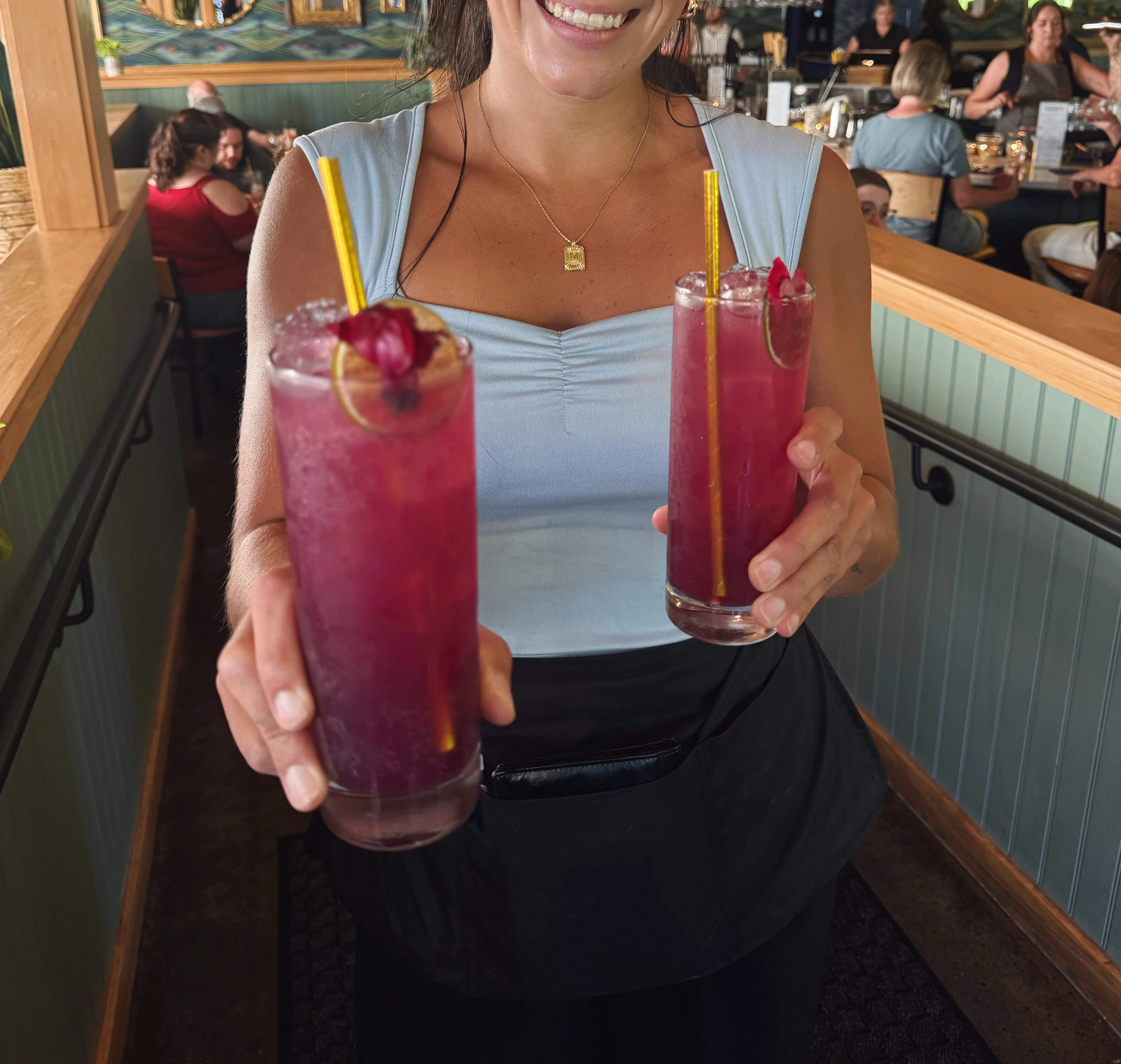 Server presenting vibrant cocktails in a lively restaurant setting