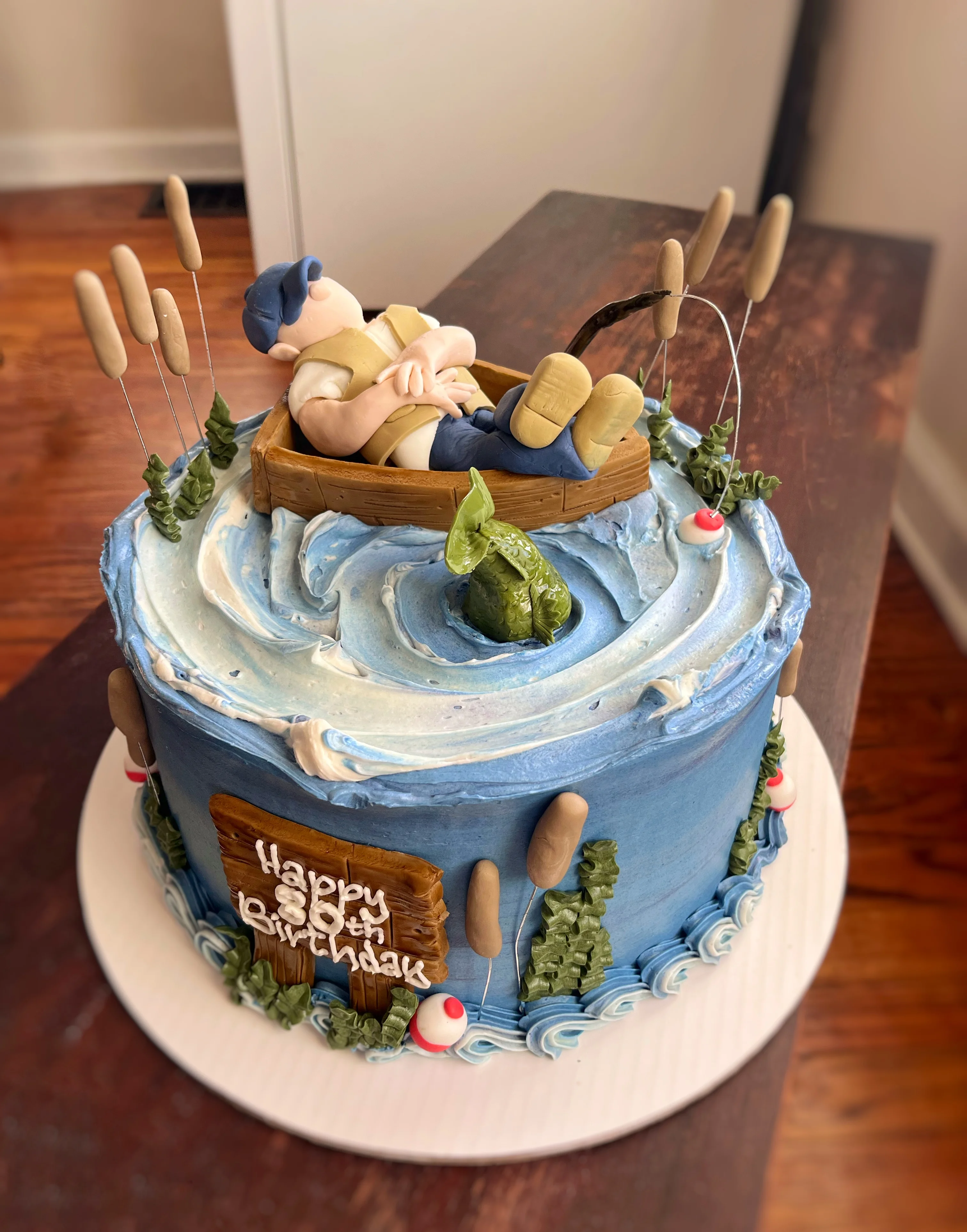 Whimsical fishing-themed birthday cake with a boat and fisherman figurine