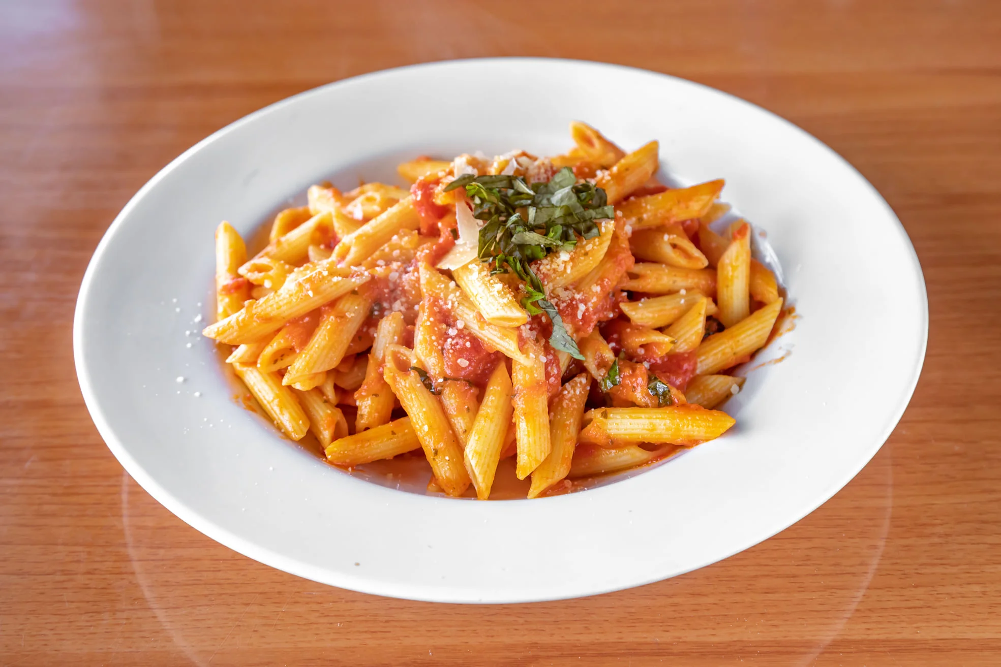 A bowl of penne pasta coated in a rich tomato sauce, topped with basil and parmesan cheese.