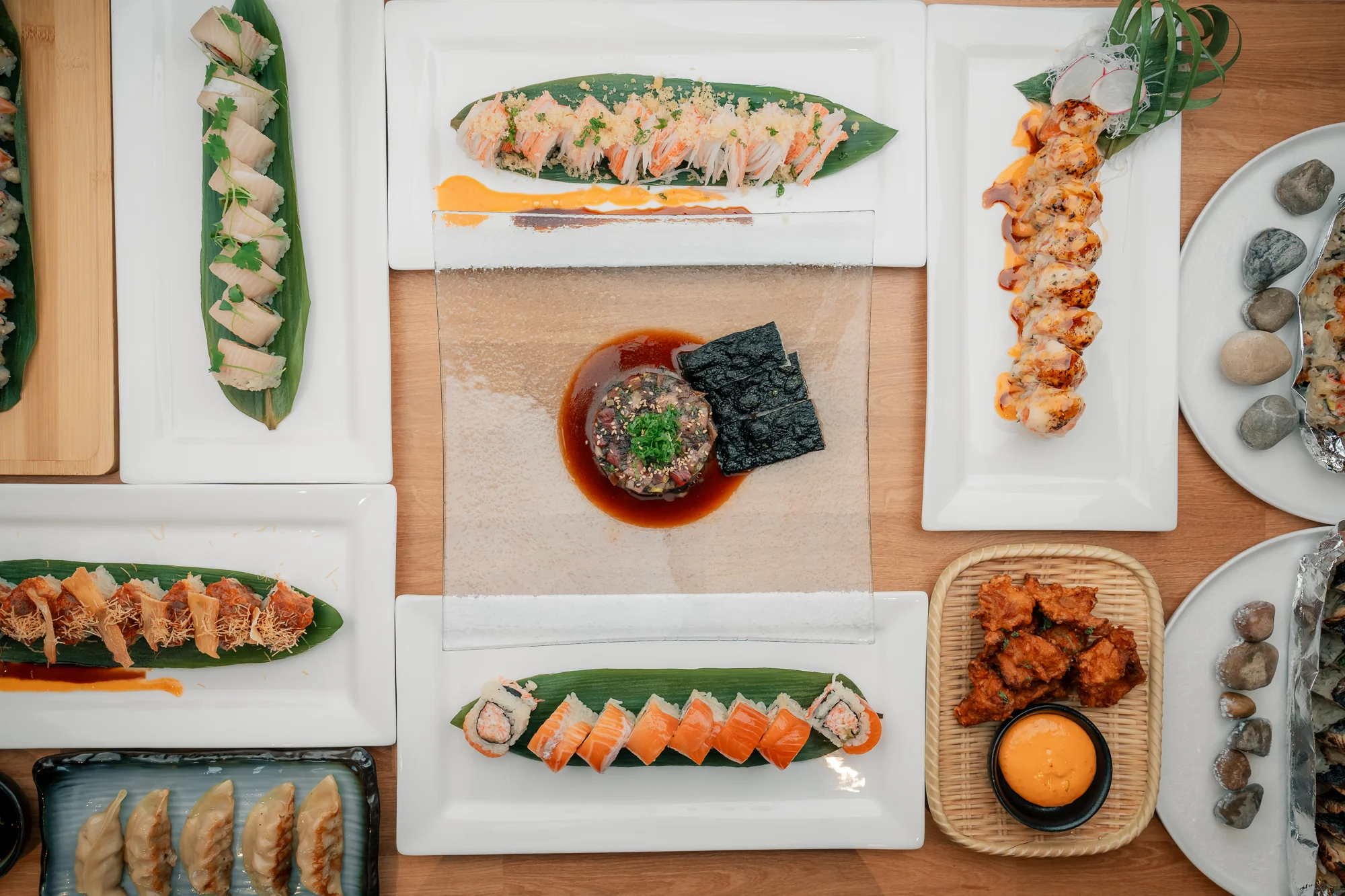 An assortment of sushi and sashimi presented on elegant white plates. The spread includes various types of rolls, garnishes, and sauces, beautifully arranged.