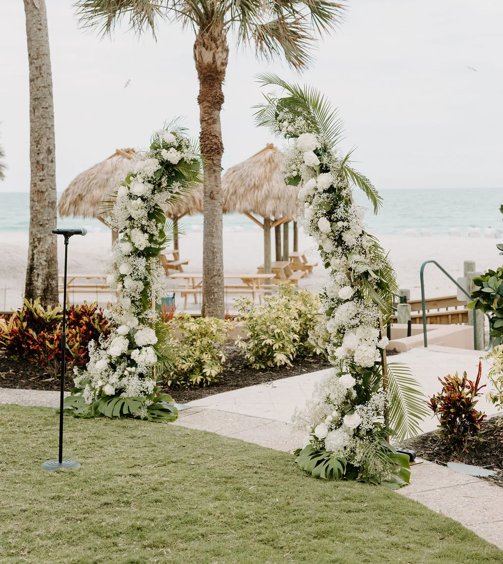 Beach wedding arch adorned with white flowers and palm trees